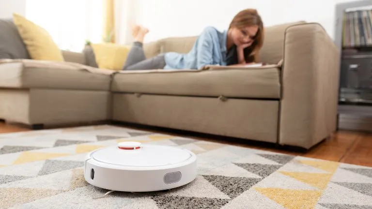mulher lendo deitada no sofá e robo aspirador limpando o tapete a frente